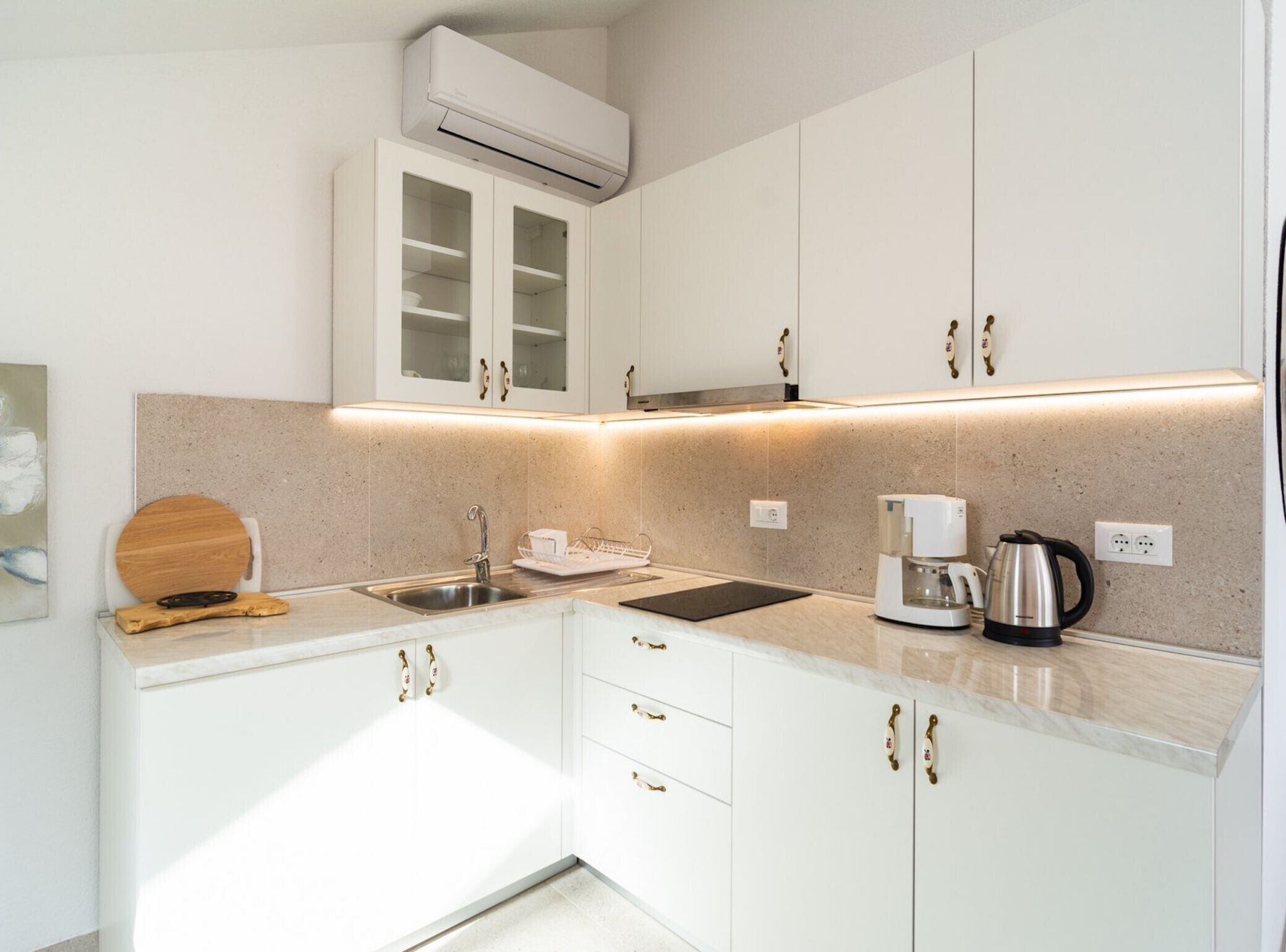 A modern kitchen with white cabinets, a built-in oven, a coffee maker, and a kettle.