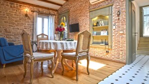 A dining area with a brick wall, wooden ceiling beams, a table with chairs, and a chandelier. - Serene Sea View Rovinj Apartment - Two Bedroom Apartment with Sea View (Rovinj)