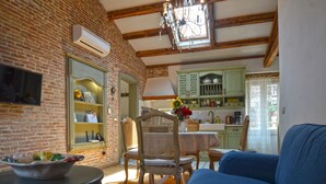 A cozy living room with a blue sofa, a dining table with chairs, a brick wall, and a kitchen in the background. - Serene Sea View Rovinj Apartment - Two Bedroom Apartment with Sea View (Rovinj)