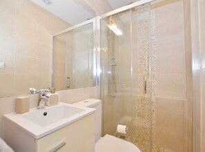 Bathroom features a large mirror, sink, and glass-enclosed shower with a pebble-textured wall and toilet paper holder.