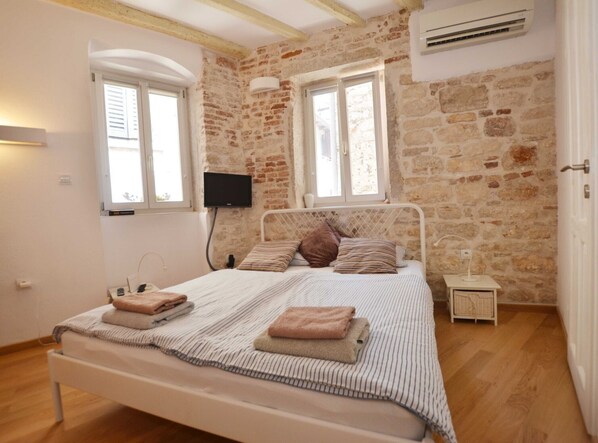 A bedroom with a stone wall, a bed with striped bedding, a flat-screen TV, and a small bedside table.