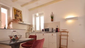 A modern kitchen with white cabinets, a dining table with two red chairs, a hanging plant, and a ladder against the wall. - Modern and Cozy Rovinj Old Town Apartments - Classic Studio Apartment (Rovinj)
