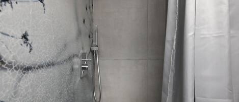 Un baño con ducha, paredes enlosadas y una cortina.