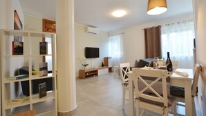 A modern living room with a TV, a dining area with a table and chairs, and a bookshelf with books. - Seaside Escape Rovinj Old Town Apartment - Three Bedroom Apartment with Sea View (Rovinj)