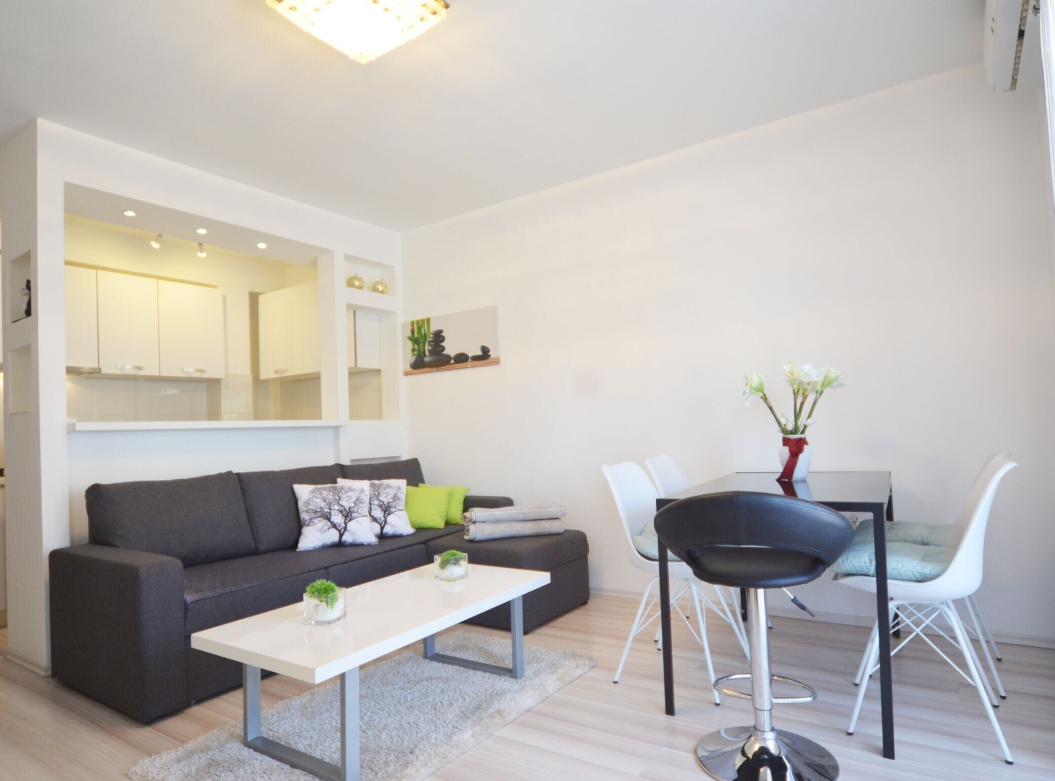 A modern living room with a grey sofa, white coffee table, and a dining area with a red vase and white chairs.