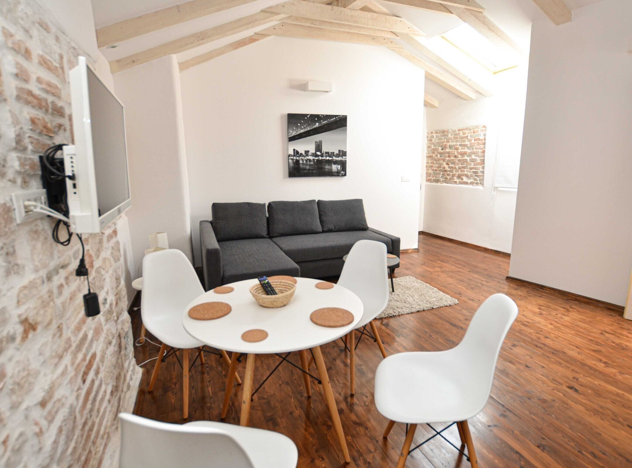 A modern living room with a grey sofa, white chairs, a round table with a basket, and a cityscape painting on the wall.