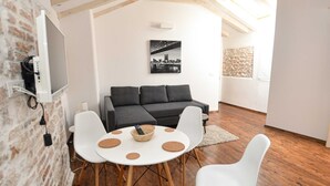 Ett modernt vardagsrum med en grå soffa, vita stolar, ett runt bord med en korg och en tavla som föreställer en stadsbild på väggen.