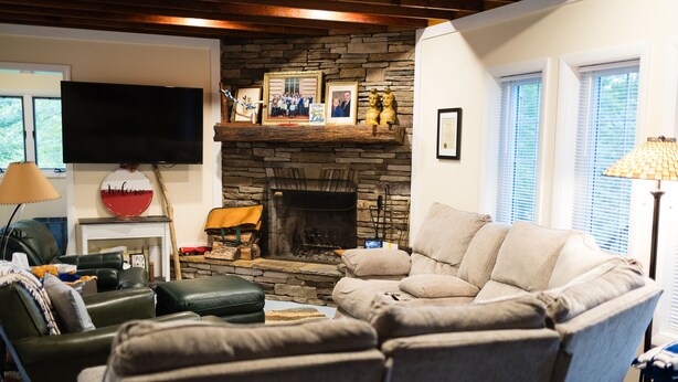 A living room with a stone fireplace, a television mounted on the wall, and a sofa. - Spacious 6-bedroom house with WiFi & AC in charming Jamestown lake ramp access (Jamestown)