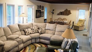 A living room with a sectional sofa, a dining table with chairs, and a lamp. - Spacious 6-bedroom house with WiFi & AC in charming Jamestown lake ramp access (Jamestown)