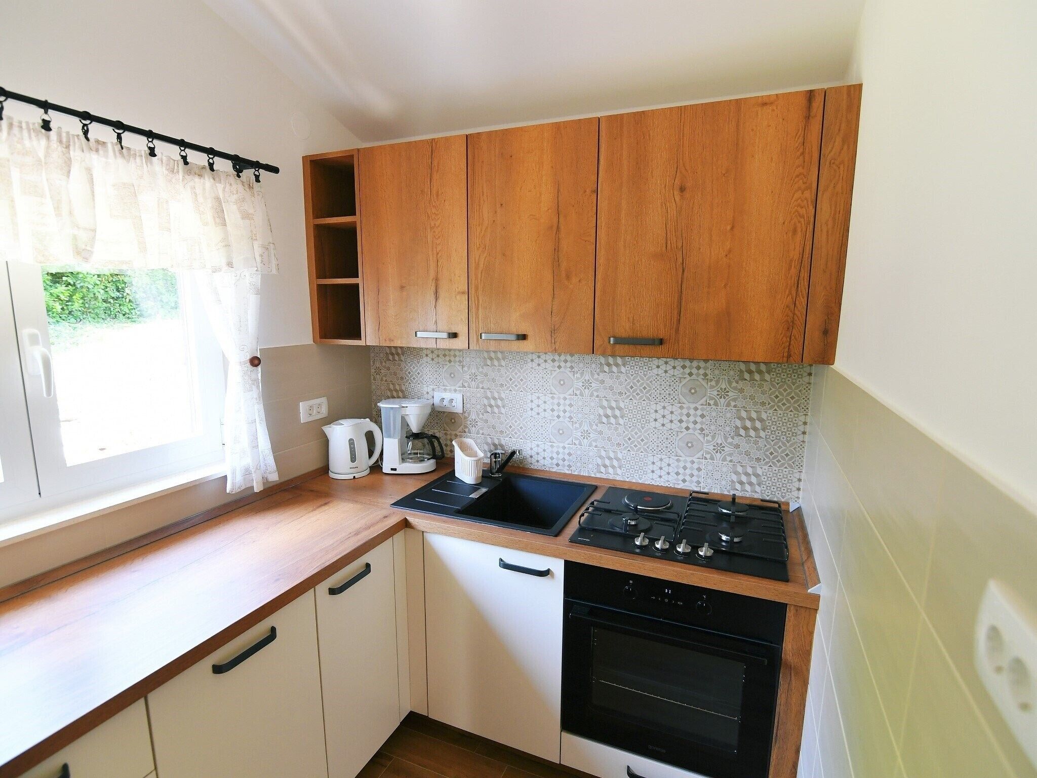 Cocina compacta con armarios de madera, cafetera, hervidor y estufa.