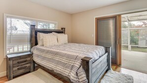 A bedroom with a bed, a nightstand, a window with blinds, and a sliding glass door. - Spacious Portland Area Home w/ Fenced Yard (Beaverton)