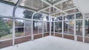 A conservatory with large glass windows and a curved ceiling, offering views of a landscaped garden. - Spacious Portland Area Home w/ Fenced Yard (Beaverton)