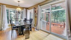 A dining area with a glass table and chairs, a hanging light fixture, and a view of a wooden deck through large glass doors. - Spacious Portland Area Home w/ Fenced Yard (Beaverton)