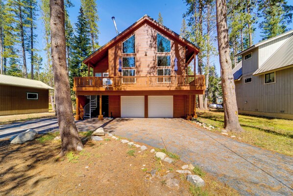 A two-story cabin with a balcony, garage, and a natural forest setting.