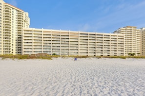 A beachfront hotel with multiple balconies, a sandy beach in front, and a clear sky.