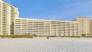 Hotel davant de la platja amb diversos balcons, platja sorrenca a l'avantguarda i cel blau clar.