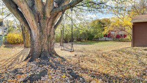 A large tree with a swing set in a yard with fallen leaves. - Game Room & Fire Pit: West Mifflin Home! (West Mifflin)