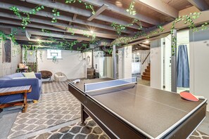Een tafeltennistafel in een kamer met een kamerbreed tapijt, een bank en hangplanten.