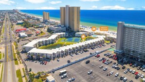 An aerial view of a coastal hotel area with multiple high-rise buildings, a parking lot, and a beach access point. - Enjoy a spacious, low-rise Sugar Beach condo with a private beach entrance, pool, sunset views, and glimpses of the Gulf. The condo sleeps up to 10 and is close to dining and local attractions in Panama City Beach. (Panama City Beach)