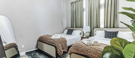 Habitación de hotel con dos camas, un espejo grande, un ventilador de techo y vistas al exterior a través de cortinas.