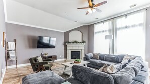 A modern living room with a fireplace, a flat-screen TV, a sofa set, and a coffee table. - Pool Volleyball Oasis |Sleeps 18 (Houston)