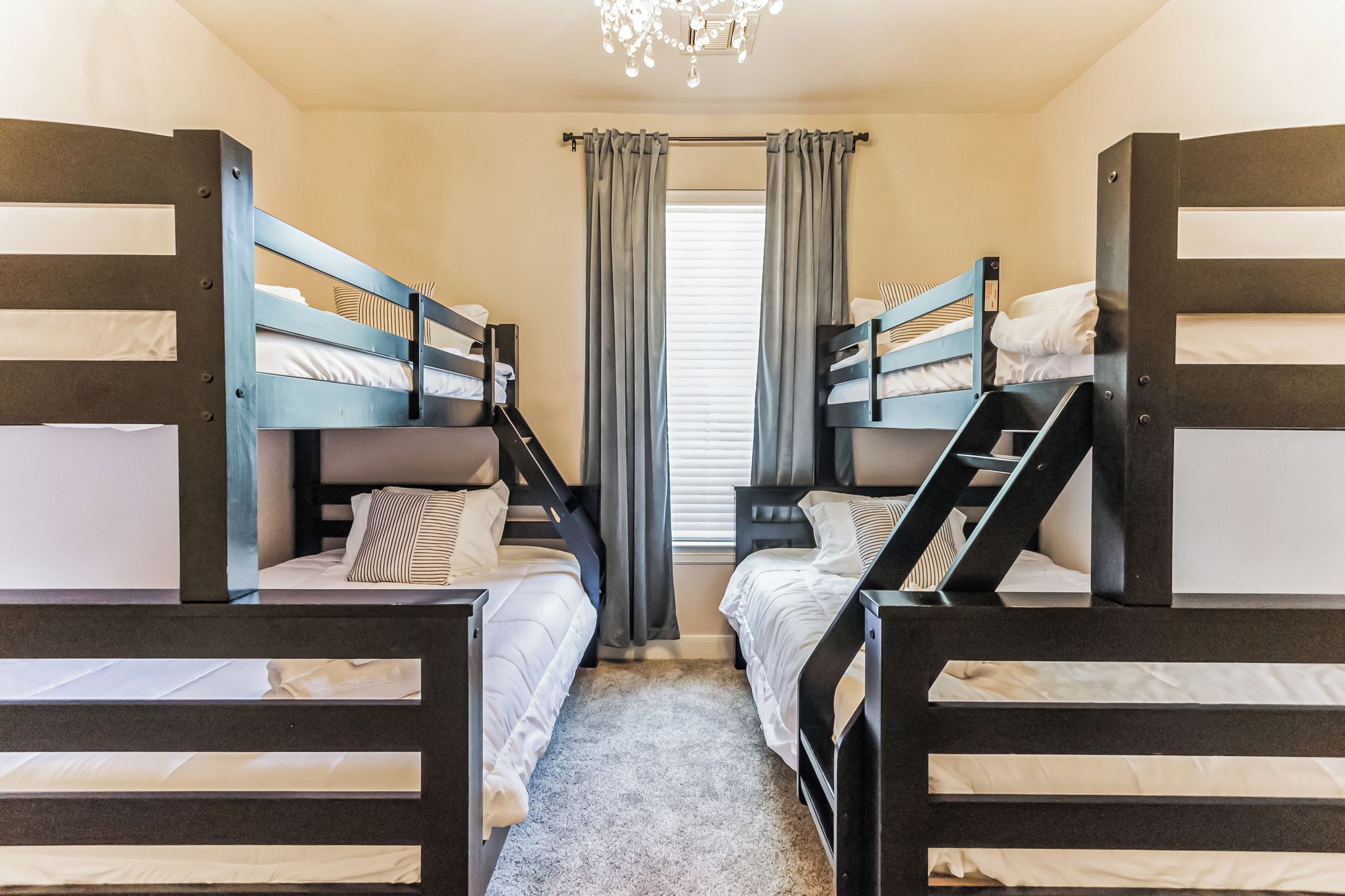 A room with bunk beds, a window with curtains, and a chandelier.