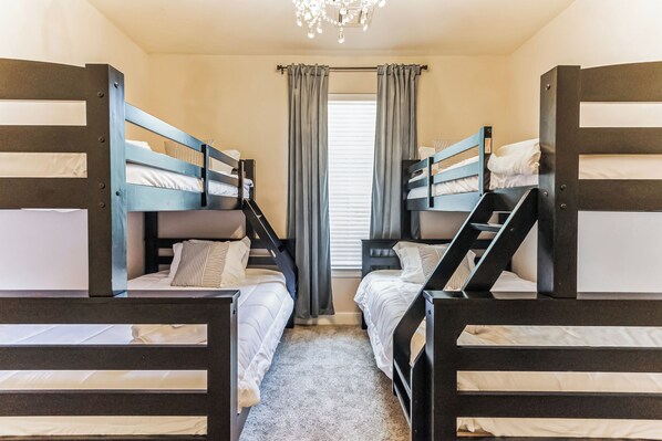 A room with bunk beds, a window with curtains, and a chandelier.