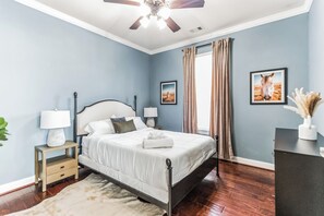 A bedroom with a bed, bedside tables, a ceiling fan, and artwork on the walls.