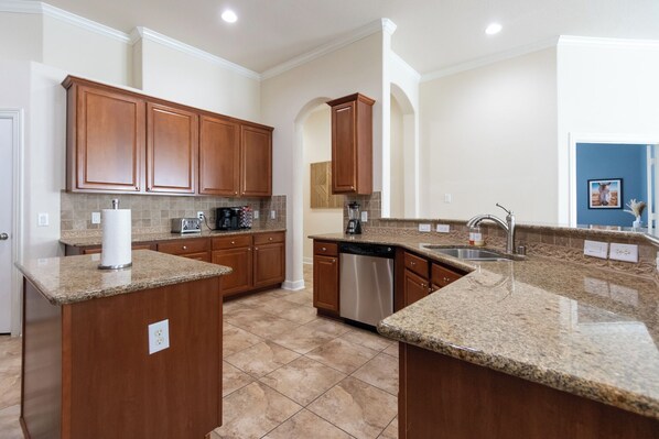 A kitchen with granite countertops, wooden cabinets, a dishwasher, and a coffee maker.
