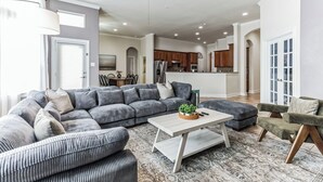 A spacious living area with a sectional sofa, a coffee table, and a dining area in the background. - Pool Volleyball Oasis |Sleeps 18 (Houston)