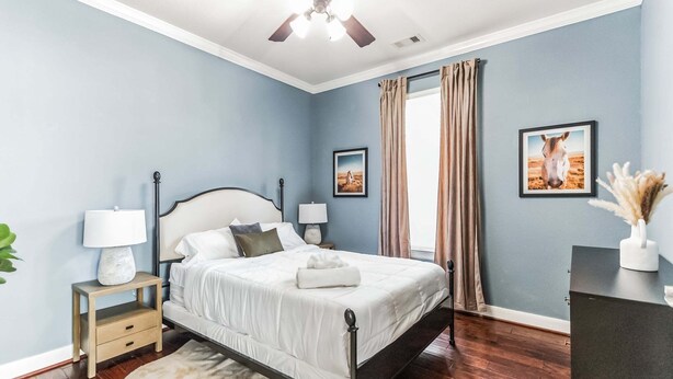 A bedroom with a bed, bedside tables, a ceiling fan, and two framed pictures on the wall. - Pool Volleyball Oasis |Sleeps 18 (Houston)