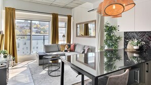 A modern living room with a glass dining table, a sofa, and a large window with curtains. - Penthouse, central Quebec city, heated pool (Québec)