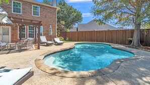 Un jardin avec une piscine, une maison en briques et une clôture en bois.