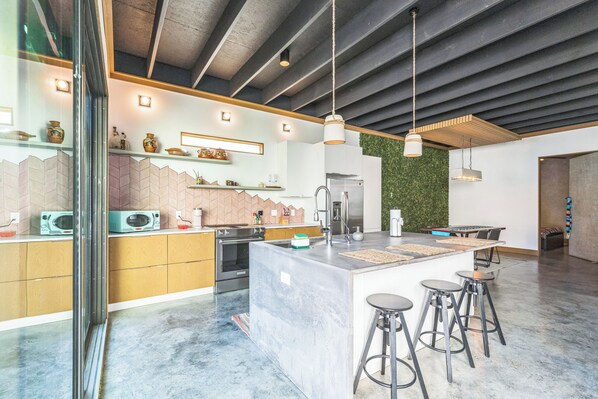 A modern kitchen with a central island, bar stools, and a green wall.
