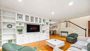 Un salon moderne doté d’un téléviseur à écran plat, d’étagères blanches et d’un escalier.
