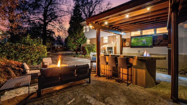 Une terrasse extérieure avec un sol en pierre, un barbecue et un coin bar équipé de tabourets.