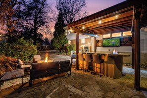 Eine Terrasse im Freien mit Steinboden, Grill und einer Bar mit Hockern.