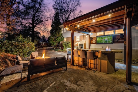 An outdoor patio with a stone floor, a barbecue grill, and a bar area with stools.