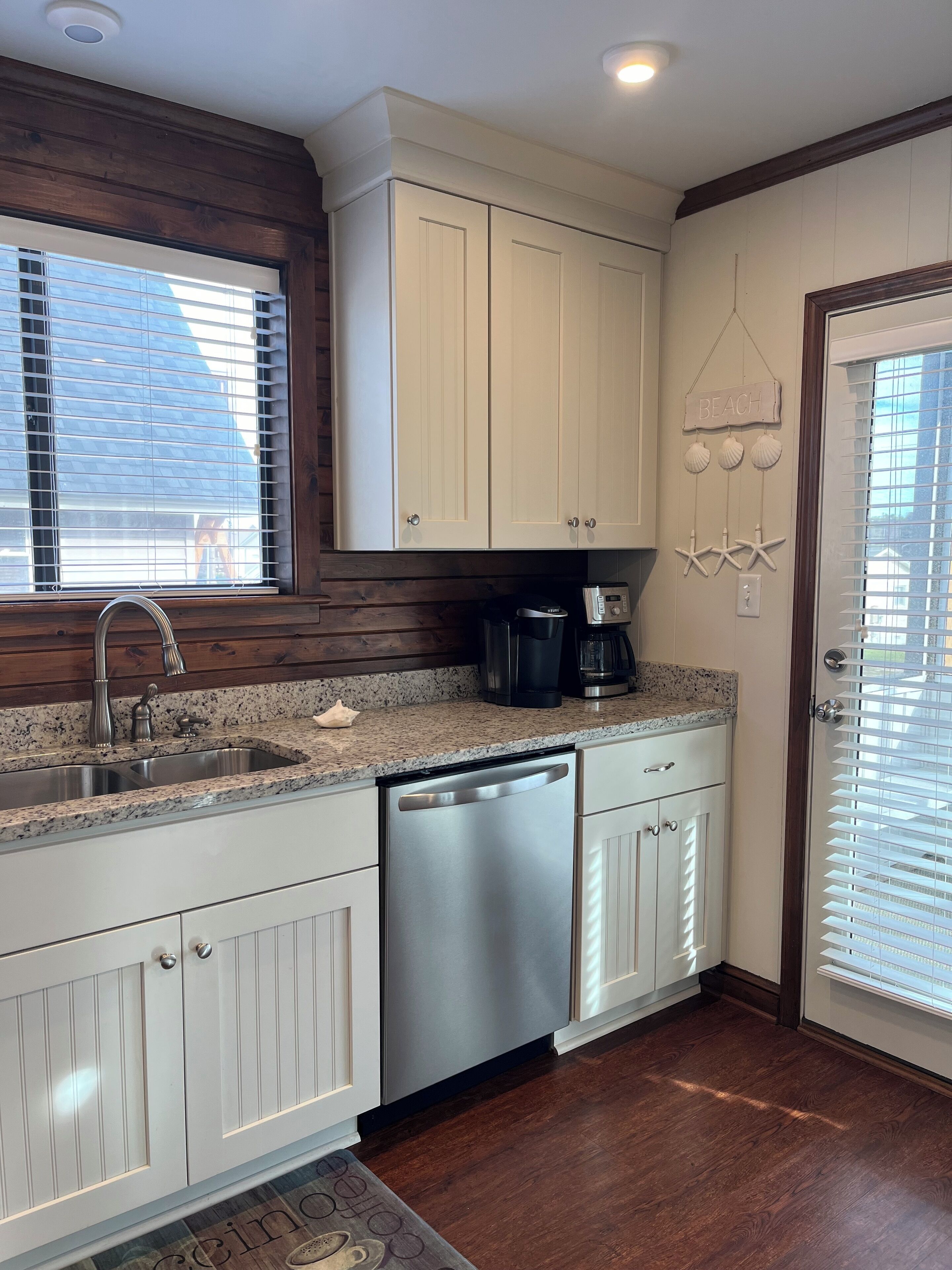 A kitchen with white cabinetry, a stainless steel dishwasher, a coffee maker, and a window with blinds.