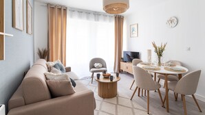 Ein modernes Wohnzimmer mit einer Couch, einem Couchtisch, einem Esstisch mit Stühlen, einem Fernseher und einer dekorativen Uhr an der Wand.
