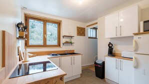A compact kitchen with white cabinets, a wooden countertop, a built-in stove, and a window providing natural light. - Les Jonquilles - 3 chambres et garage privé (Cornimont)