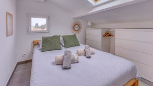 A bedroom with a skylight, a bed with rolled towels, a dresser, and a hanging rack.
