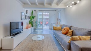 A modern living room with a flat-screen TV, a grey sofa, and a white coffee table.