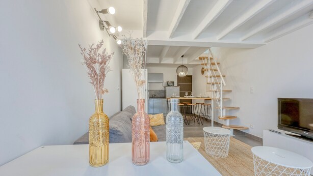 A modern living room with a white sofa, a coffee table with decorative bottles, a TV, and a staircase leading to an upper level.