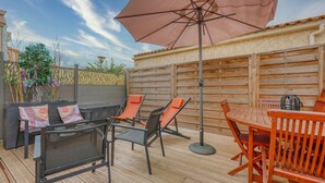 An outdoor patio with a wooden table and chairs, a large umbrella, and a seating area with cushions.