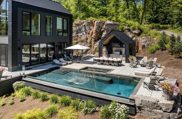 A modern outdoor pool area with lounge chairs and a barbecue station, surrounded by natural rock formations and greenery.