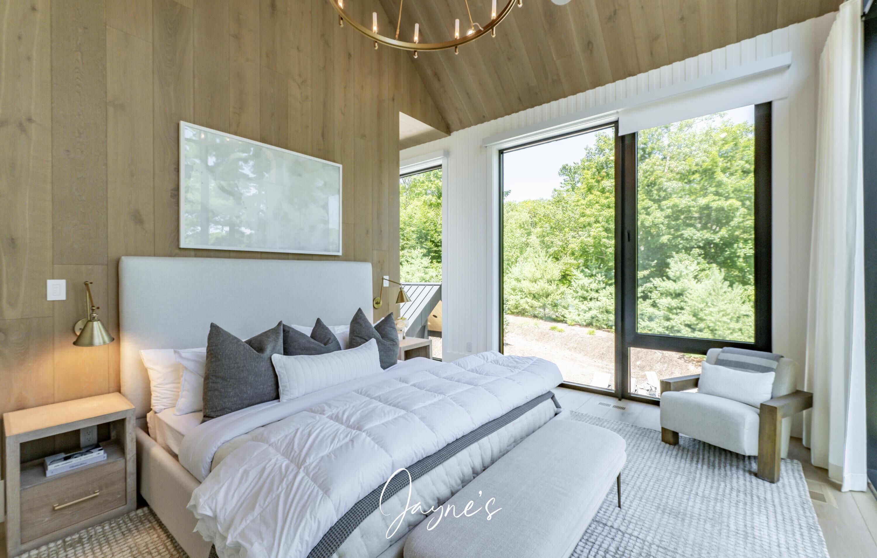 A modern bedroom with a large bed, a bedside table, a chair, and a view of the outdoors.