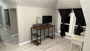 Una habitación con un escritorio de madera, televisor y una ventana con cortinas negras.