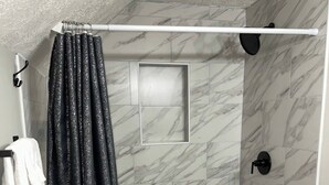 Zona de ducha con un cabezal blanco, cortina de ducha negra y paredes con estampado de mármol.