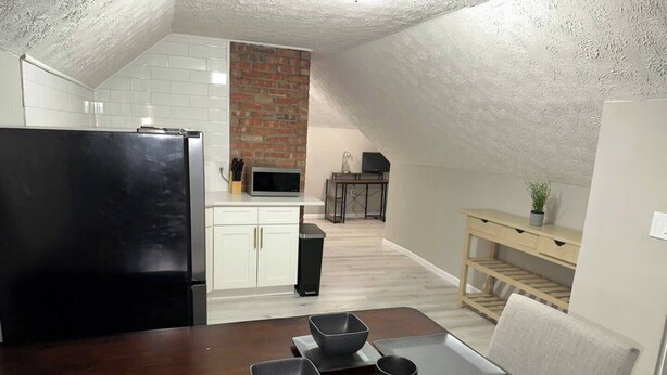 Una cocina compacta con armarios blancos, pared de ladrillo y comedor con mesa de madera oscura y cuencos grises.